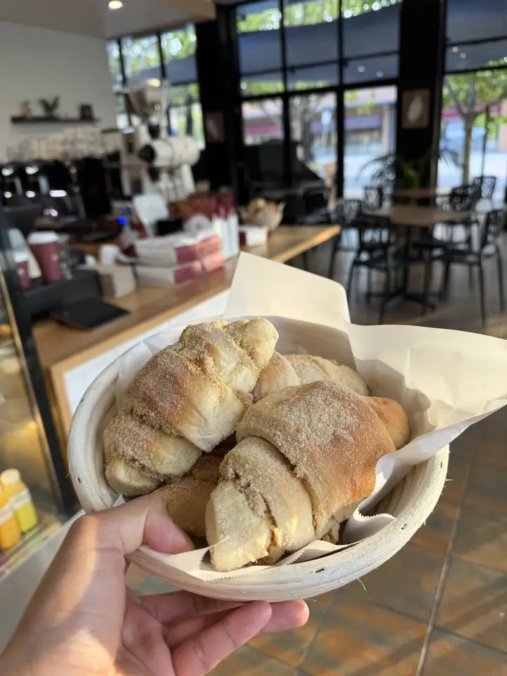 A basket of fresh bread rolls coated in breadcrumbs, held up inside the café
